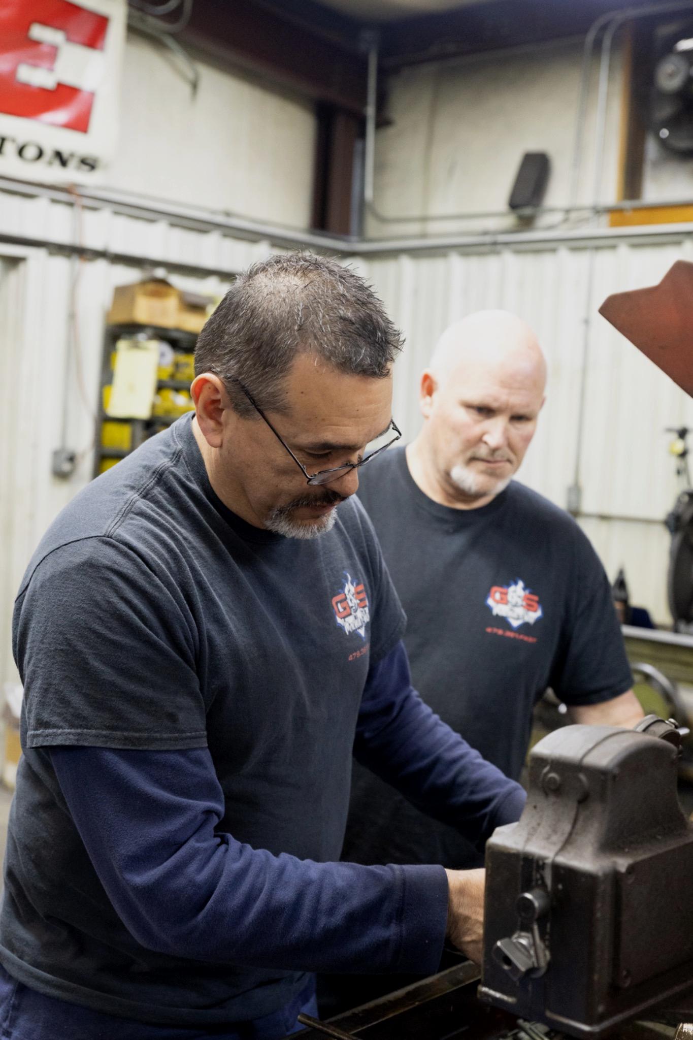 Two machinists resizing connecting rods using precision equipment at G&S Machine Shop
