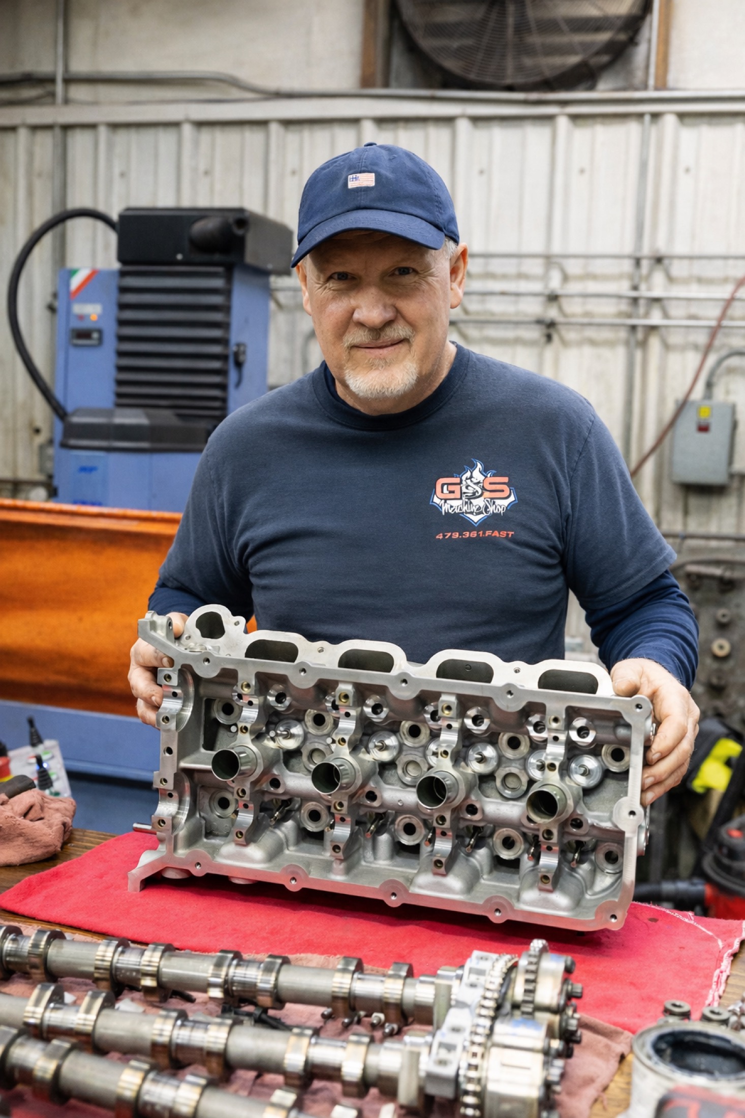 Technician holding freshly machined cylinder head during resurfacing at automotive machine shop