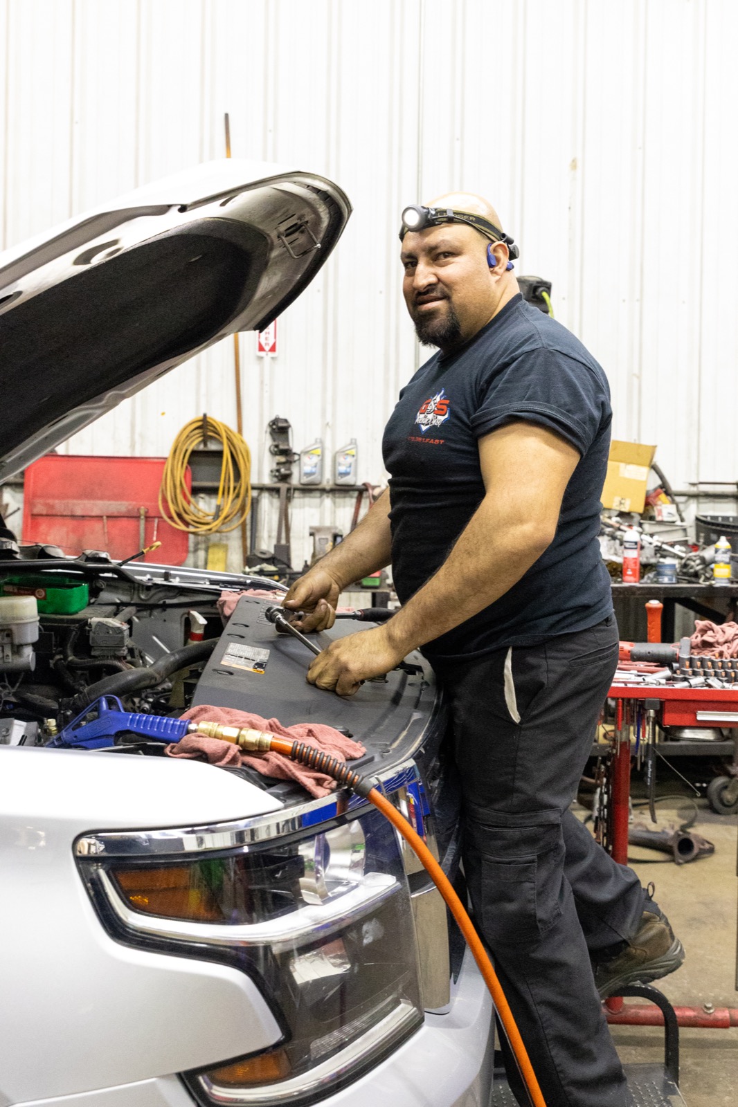 Miguel performing automotive repair on a GMC vehicle using professional shop tools