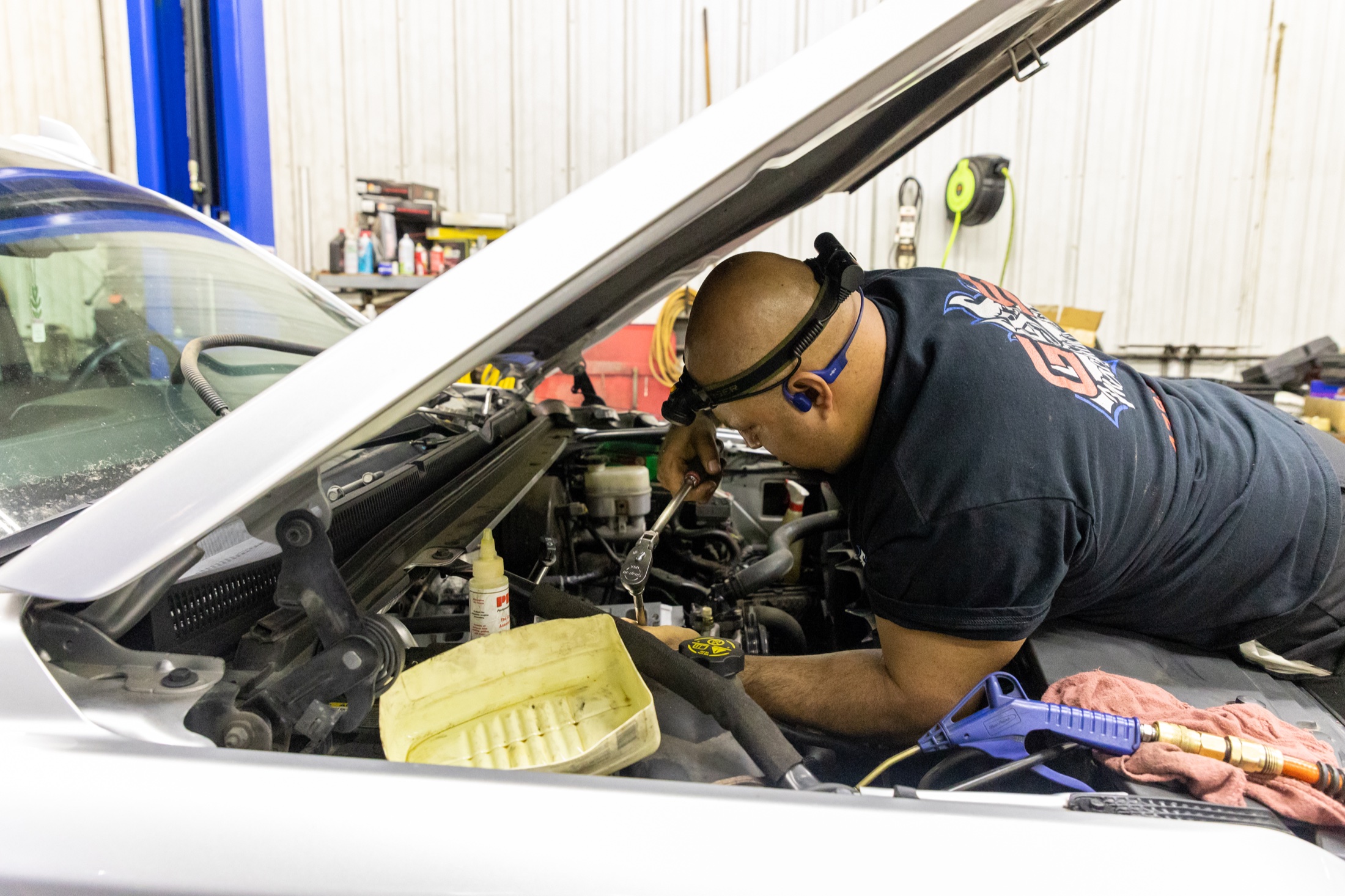 Miguel tightening engine components under the hood during automotive repair on a customer vehicle