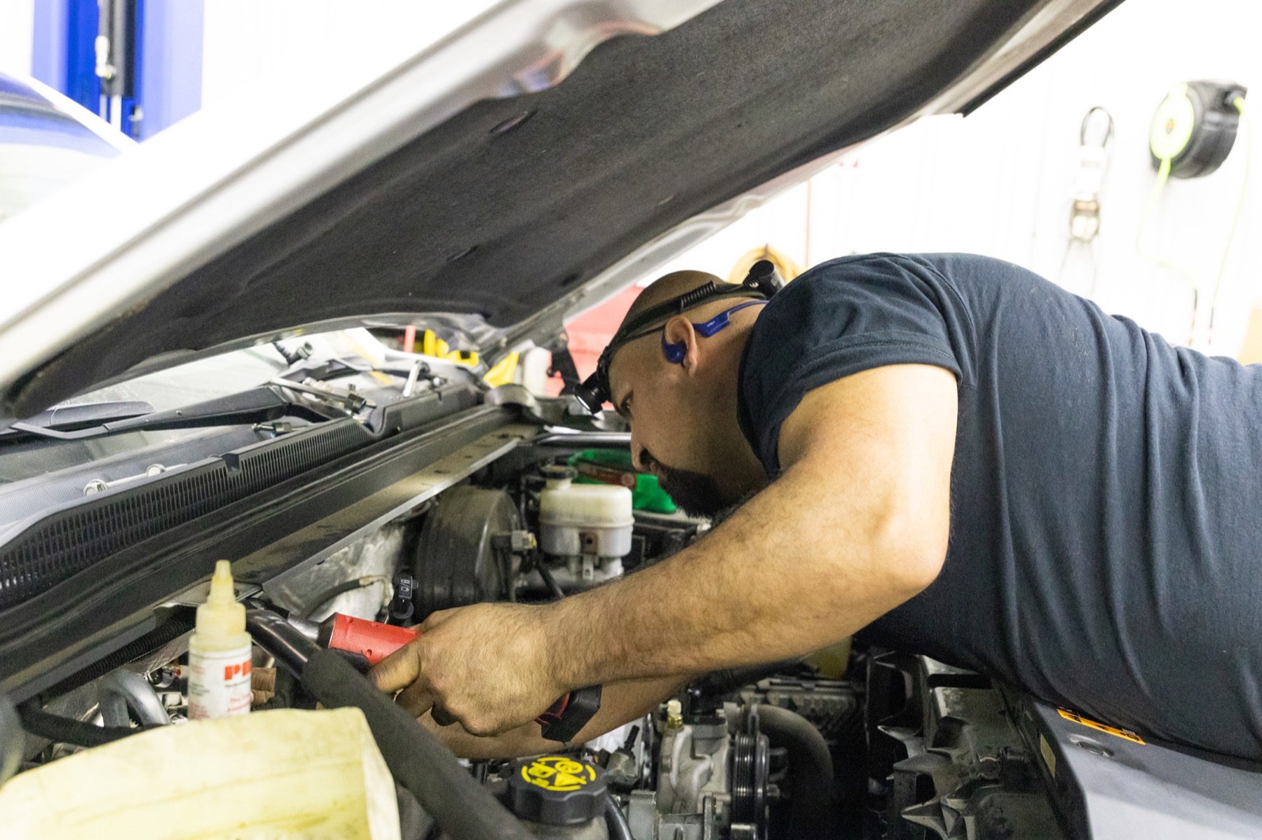 Miguel working under the hood performing automotive repair on a customer vehicle